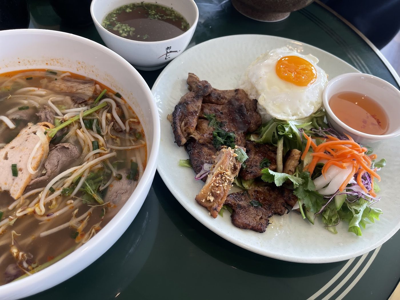 Pho beside a grilled plate with rice, egg, vegetables and dipping sauce